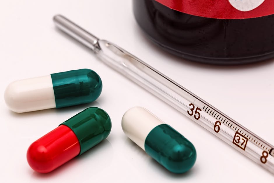 green red and white pills with a thermometer on table