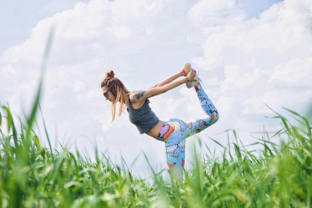 girl in the grass doing yoga wearing printed pants and a crop shirt