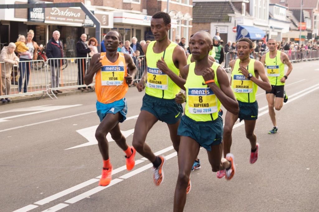 marathon runners with yellow tank tops wearing bib numbers