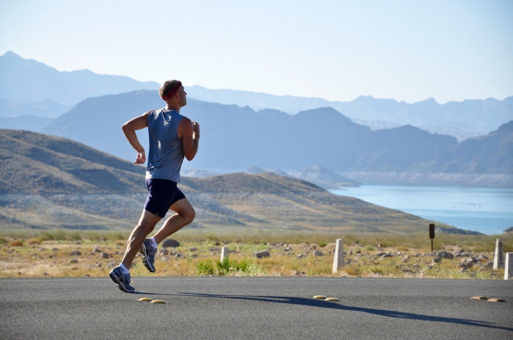 man running in shorts and tank top with headband near lake with mountains