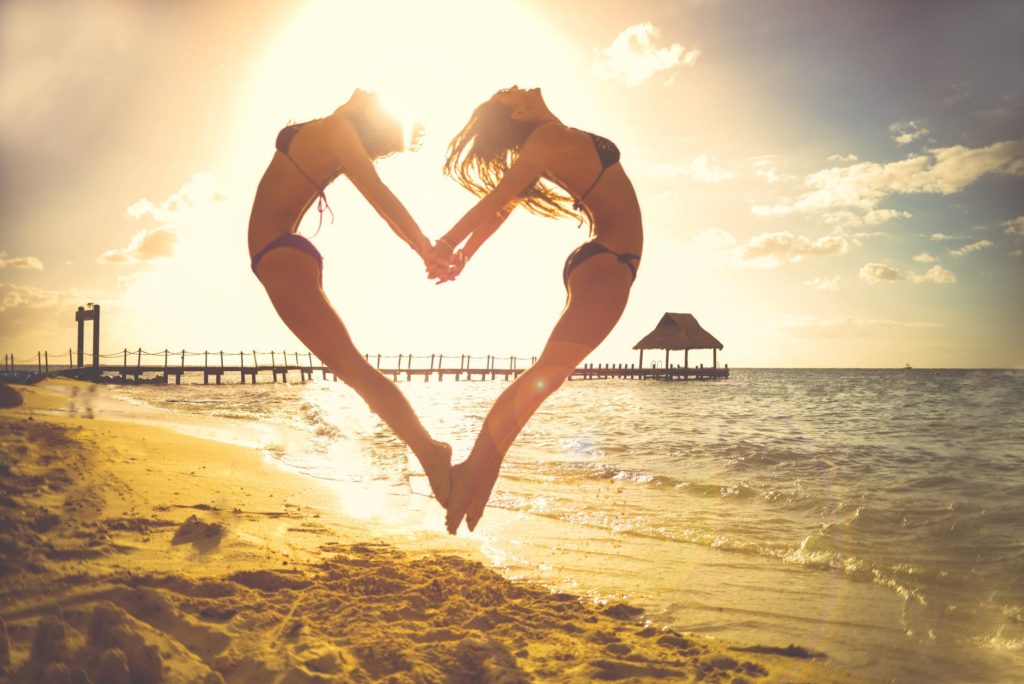 two girls in bikinis jumping to form a heart with their bodies