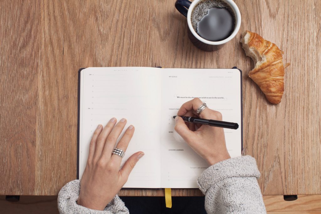 female arms writing in journal with coffee and croissant 