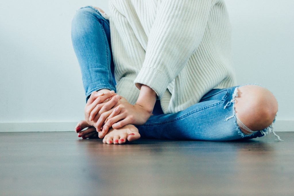 female sitting on the floor in jeans, a white sweater and bare feet