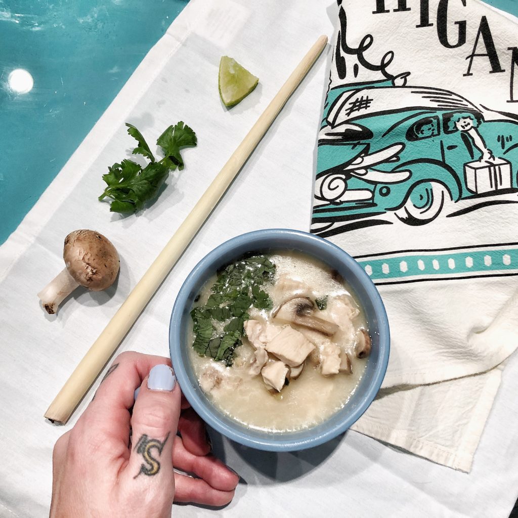 thai chicken coconut soup in blue bowl with hand