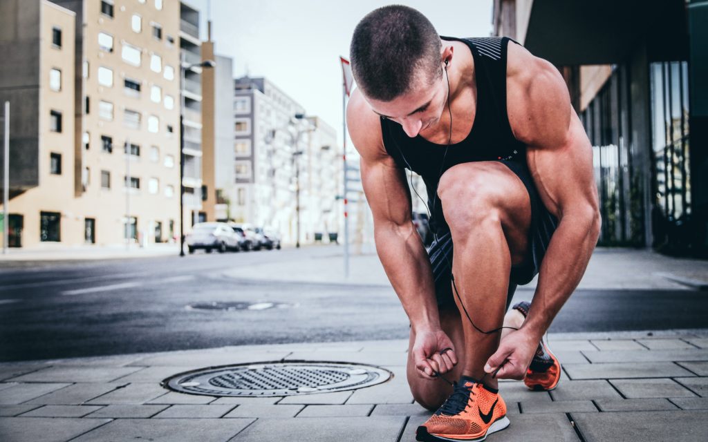 muscular man kneeling down to tie running shoes with earbuds on