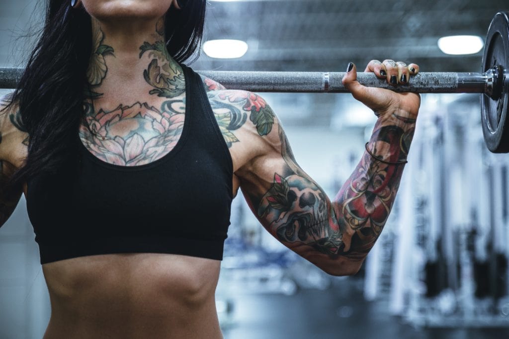 girl with tattoos working out with barbell on back