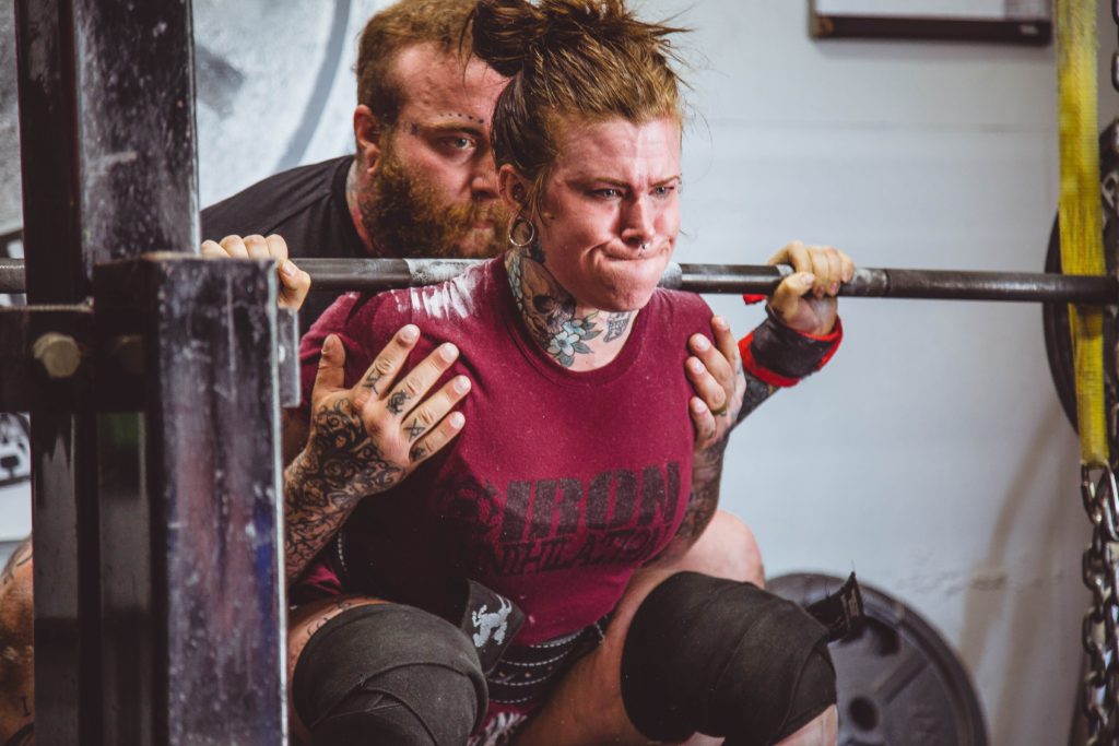 female lifting heave weight with a barbell with a male spotter