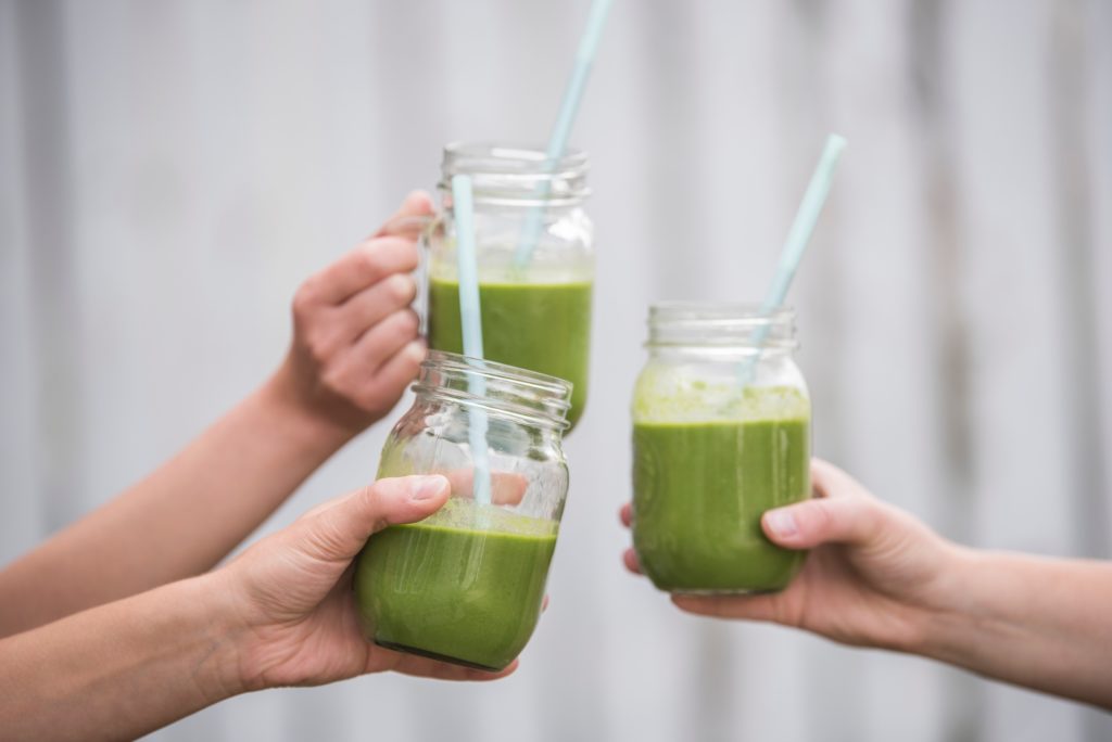 3 green smoothies in glasses with straws, cheers