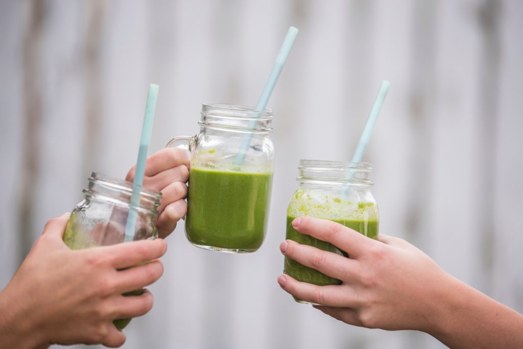 three green smoothies in mason jars with straws